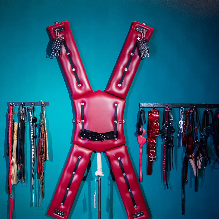 Studioeinrichtung mit gepolsterter Andreaskreuz-Wand und BDSM-Equipment im Golden Cage in NRW.